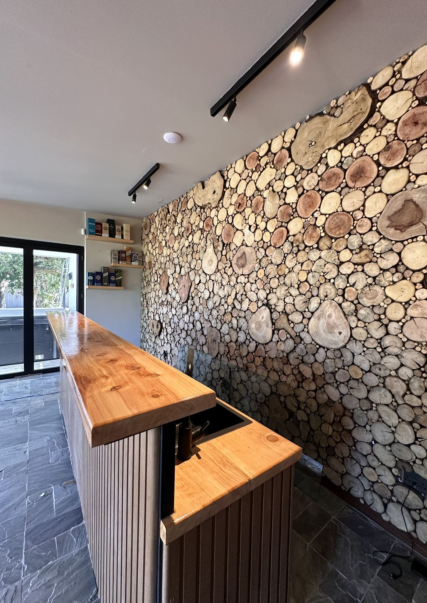 Custom outhouse entertainment space with log-slice feature wall and slatted bar